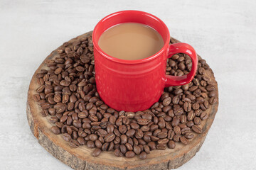 Red cup of coffee with coffee beans on wood piece