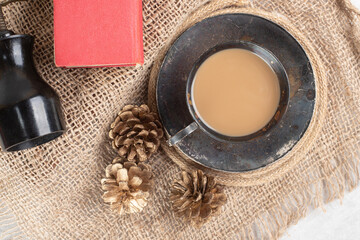 Cup of coffee, pinecones and book on burlap