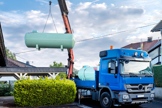 Delivery and installation of a large liquid gas tank in the garden of a residential area. Crane lifts tank into garden