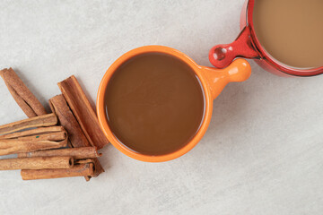 Two cups of coffee and cinnamon sticks on marble surface