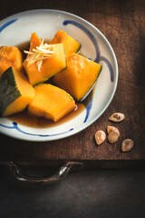  Autumnal  Kabocha Squash (Japanese Pumpkin) recipe. Japanese Simmered Kabocha cooked in savory dashi broth seasoned with soy sauce and sake with pumpkin seeds, close up, wooden rustic background