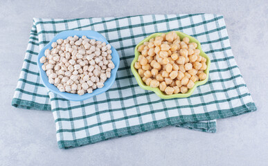 Platters filled with raw and cooked chickpeas on marble background