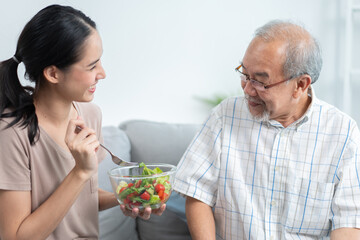 Young Asian daughter serving and feeding food to senior father in the living room. family love and support to patient grandfather. take care happy old man at home.