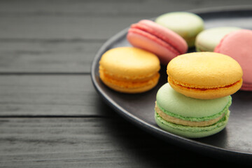 Colorful macarons cakes on black background. Small French cakes on plate. Space for text