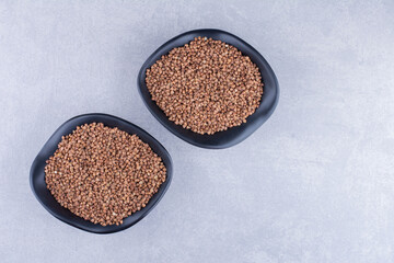 Two bowls of raw buckwheat on marble background