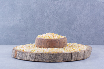 Brown rice piled on a slice of log with a full bowl in the middle, on marble background