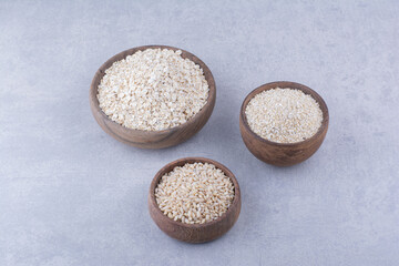 Wooden bowls filled with rice, oat and oat flakes on marble background