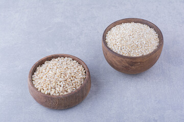 Wooden bowls filled with short-grain rice and oats on marble background