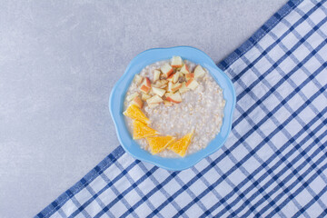 Small bowl of oatmeal on a towel topped with chopped apple and orange bits, on marble background