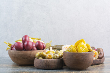 Salty vegetables in wooden bowls on marble background