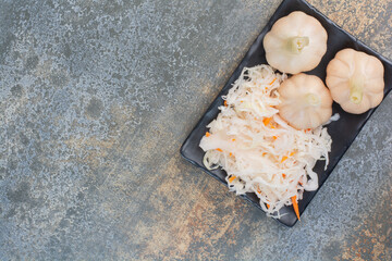 A dark plate full of salty cabbage and garlics on white background
