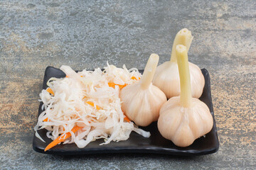 A dark plate full of salty cabbage and garlics on white background