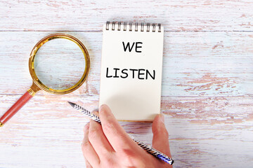 A man's hand holds a notebook with the inscription we listen