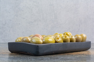 A dark board of some salty delicious olives on marble background
