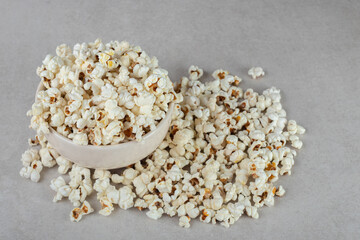 Overfilled white bowl next to a messy pile of popcorn on marble background