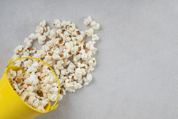Small yellow bucket pouring out fresh popcorn on marble background
