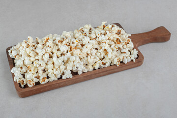 Wooden tray with a handle stocked with a portion of popcorn on marble background