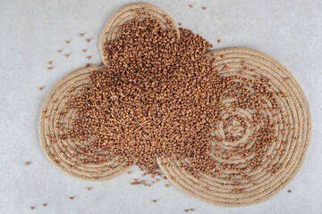 Three trivets of various sizes underneath a scattered pile of buckwheat on marble background