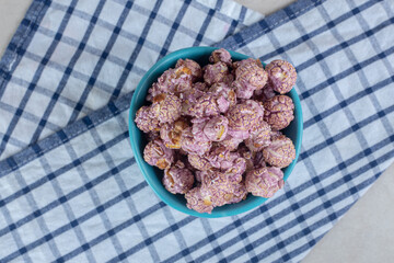 Blue bowl resting on a folded towel and filled with candy coated popcorn on marble background