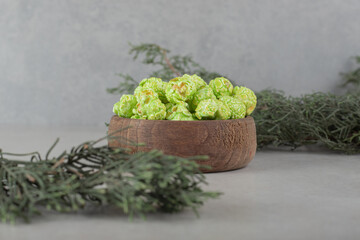 Decorative evergreen branches with a bowl of popcorn candy in the middle on marble background