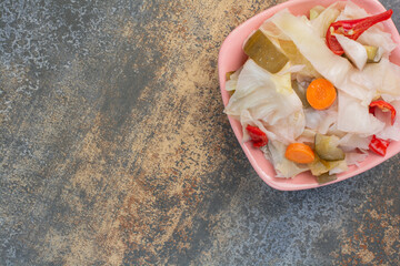 A pink plate full of salty vegetables on marble background