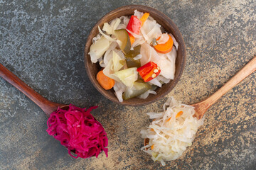 Two spoons of cabbage with wooden bowl of salty vegetables