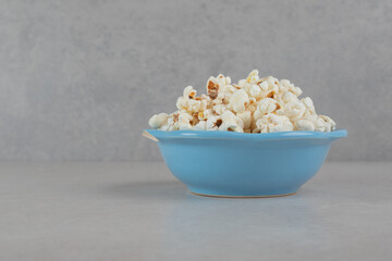 Blue bowl stocked with fresh popcorn on marble background