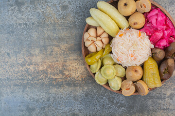 Salty vegetables in wooden bowl on marble background