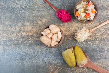 Three spoons of cabbage with wooden bowl of salty vegetables