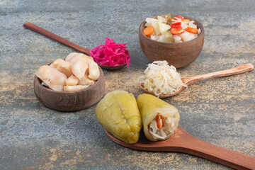 Three spoons of cabbage with wooden bowl of salty vegetables