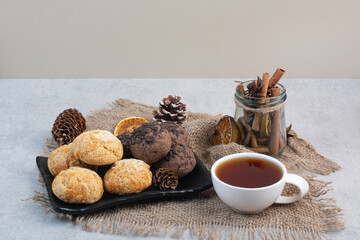 Cookies plate, tea, cinnamons and pinecones on burlap