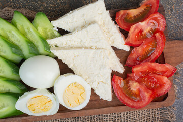 Cheese, tomatoes, boiled eggs and cucumbers on wooden board