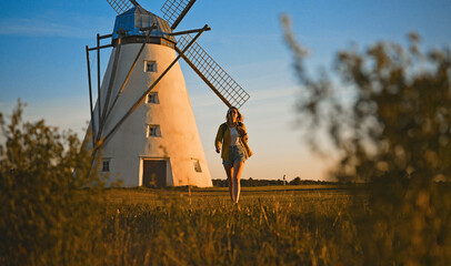 Woman with backpack walks past windmill.