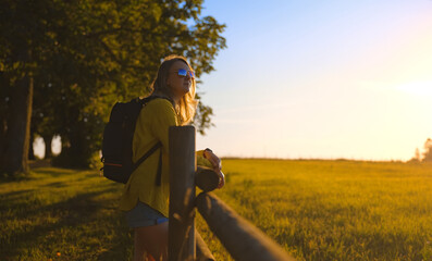 Woman with backpack looks at the sunset. Ecotourism concept.