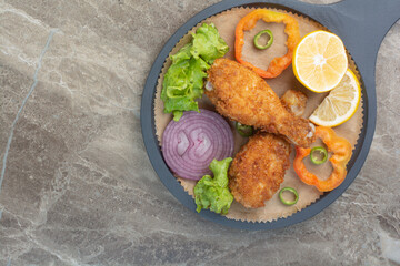 A dark pan full of fried chicken with lemon and onion