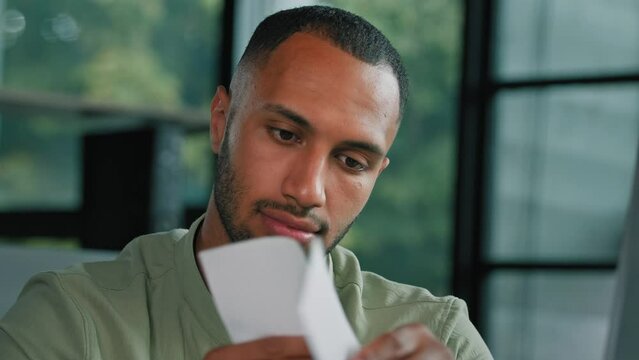 Overjoyed African Latin guy man student entrepreneur open envelope reading good news in paper admission letter at home office happy euphoric business mail notice celebrate loan approval get new job