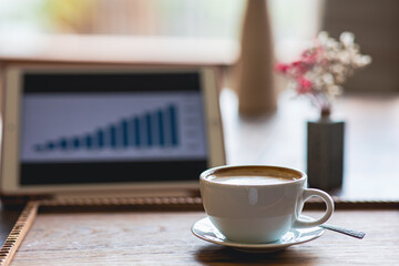 Tablet and cup of coffee on vintage colored wooden table.