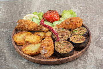 Fried chicken legs with potato and eggplant on wooden board