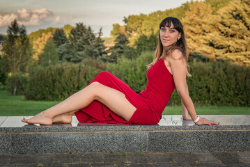 Portrait of a young beautiful dark-haired girl in a red dress in nature.