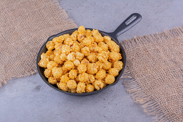 Fabric pieces underneath a pan filled with caramel flavored popcorn on marble background