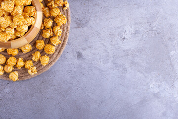 Caramel popcorn filling and ringed around a wooden bowl on marble background