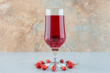 Glass of red juice with rosehips on blue table
