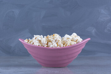 Purple bowl filled with crunchy popcorn on marble background