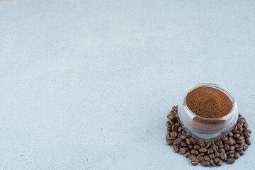 Glass of ground coffee and coffee beans on blue background