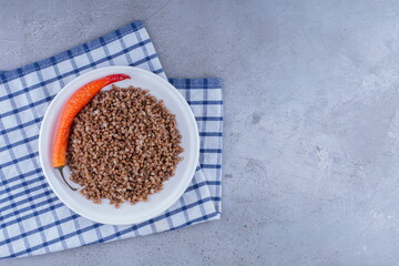 Plate of buckwheat with pepper on a towel on marble background