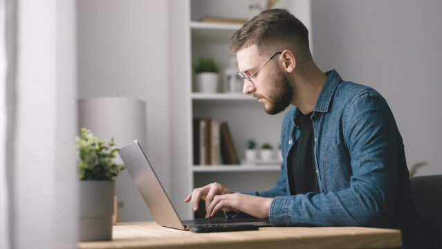 Handsome bearded man typing on laptop, young coder writing code, home office light interior