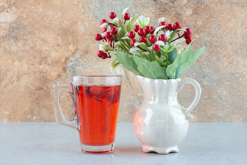 Glass of juice with rosehips and artificial flowers on blue table