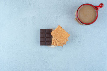 Cup of coffee, biscuits and chocolate bar on blue surface