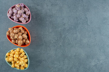 An assorted variety of popcorn candy colors assorted in small bowls on marble background