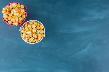 Two buckets filled with caramel coated popcorn on blue background